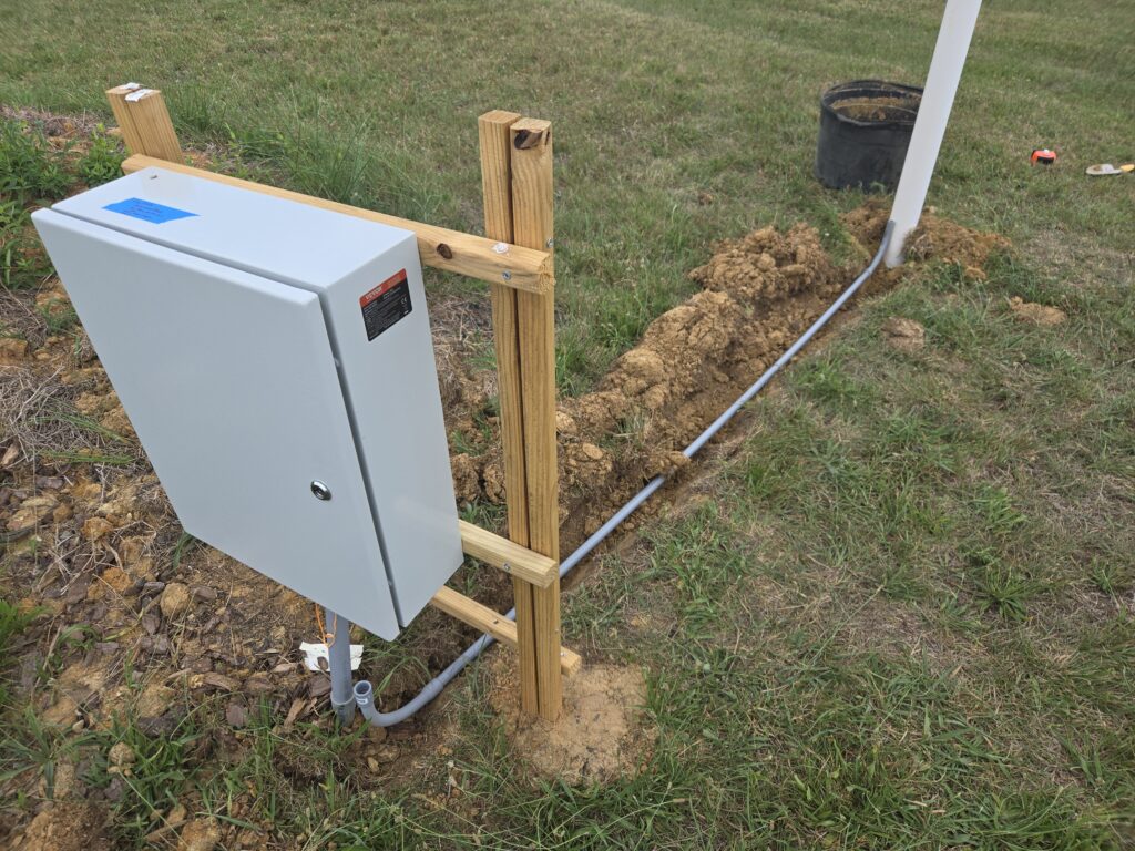 Control panel, with trench and conduit running to a white vertical pipe.